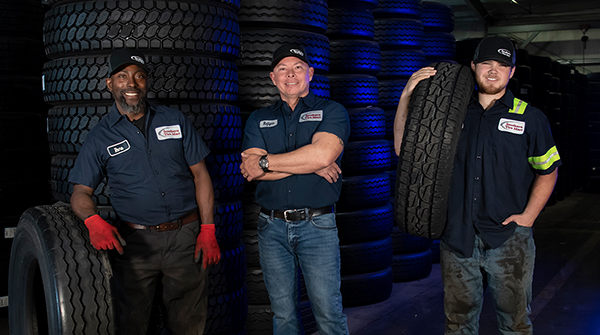 Three mechanics stand posing for picture in front of tires