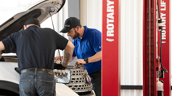 Two mechanics working on the engine of a retail vehicle